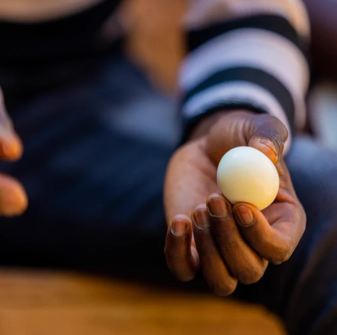 A hand clad in a black and white striped long-sleeved-tee-shirt holds an egg.