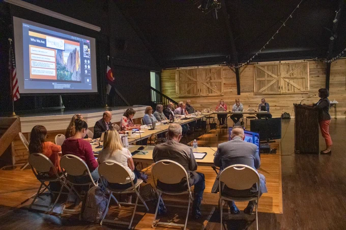 The Pikes Peak Area Council of Governments' Board of Directors sit around a U-shaped table while a person presents at a podium.