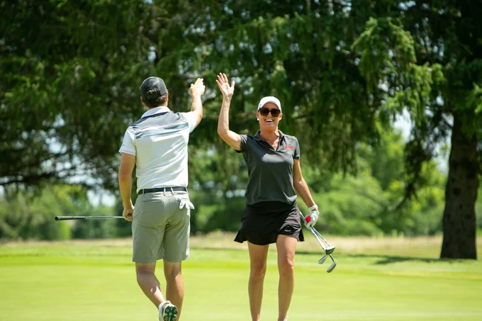 Two golfers high five and smile.