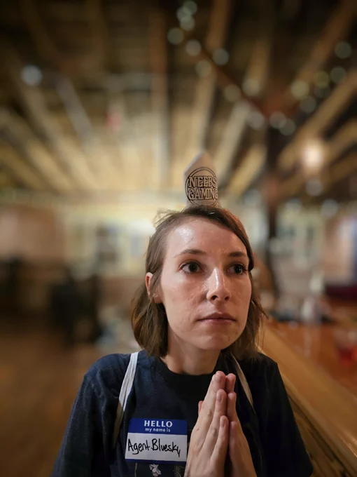Woman stands with hands in prayer with a napkin pope hat that says Neebs Gaming