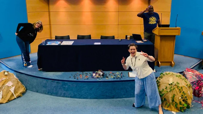 Deborah and Gemma grinning at the camera in front of a panel table on a stage.  There are decorated umbrellas on the floor.