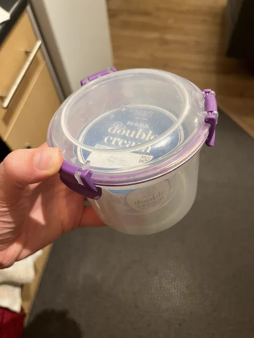 A small pot of double cream secured in a round Tupperware that is just the right size for it.