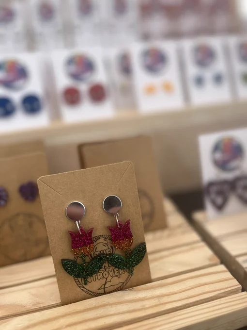 A pair a resin earrings that I made. The top part of the flower is sparkly pink which blends into gold. The stem and leaves of the flowers are green.