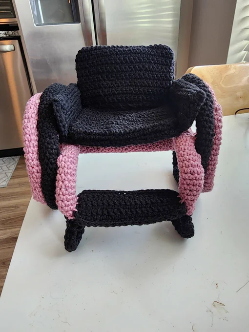 A front view of a crochet black and pink wheelchair