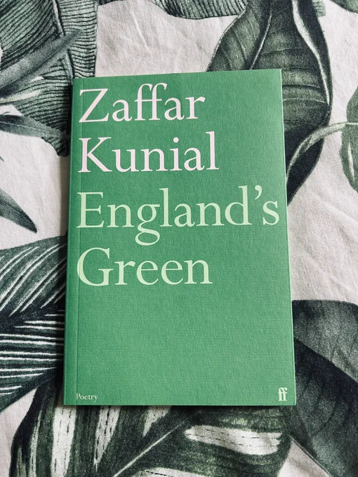 A green book with white and light green text is placed on a white fabric depicting dark green leaves.
