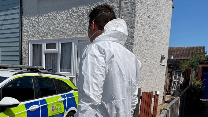 An officer in a white forensic suit outside a house.