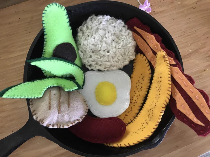 Cast iron skillet with Colombian dish Bandeja Paisa made out of felt: fried egg, avocado, arepa, plantains, salt pork, and chorizo
