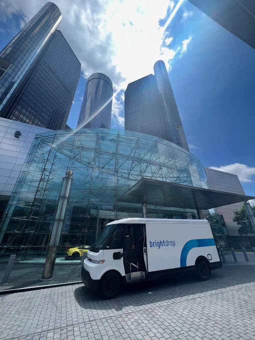 The BrightDrop Zevo 600 delivery van sits parked in front of a glass building with the sun shining.
