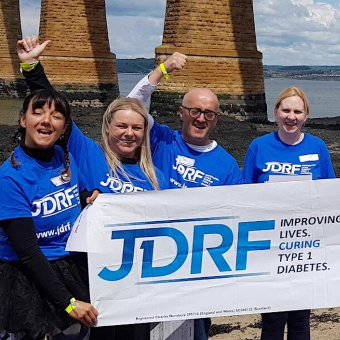 Four people cheering and holding a JDRF banner underneath the bridge.
