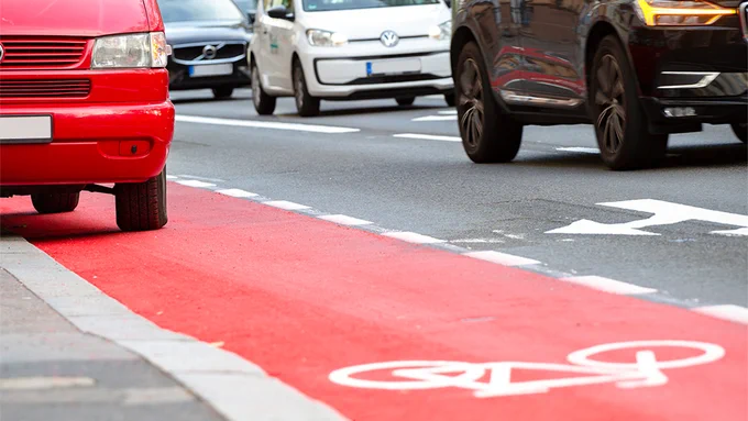 Ein Auto steht auf einem Radfahrstreifen. Neben dem Radfahrstreifen befindet sich eine vielbefahrene Straße.