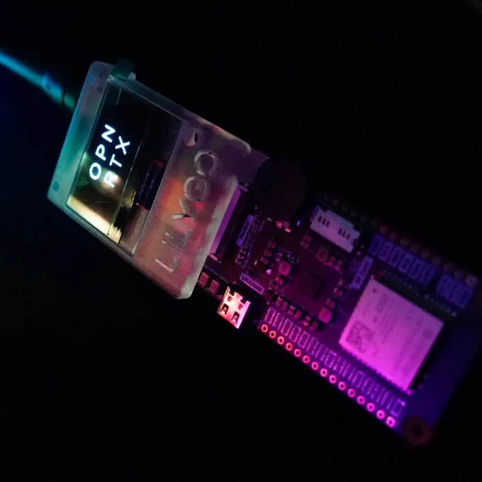 Picture of a LILYGO T-TWR Plus Open Edition on a dark background, lit by an RGB rainbow light, showing OpenRTX splash screen.