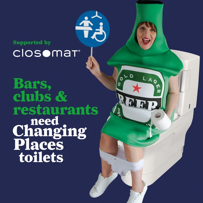 Female on a Closomat Wash & Dry toilet dressed as bottle of beer, white pants around lower leg, with Changing Places sign. Supported by Closomat. Bars, clubs & restaurants need Changing Places toilets