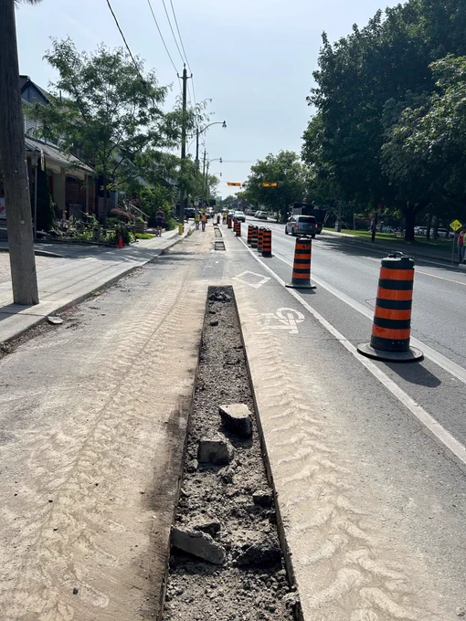 A section of roadway is cut to indicate the location of future concrete curbs between the bikeway and on-street parking on Dundas Street East.