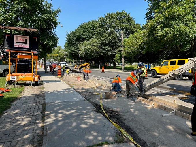 Construction workers pour concrete into wood frames separating the area of a future bike lane and motor vehicle traffic lane, which will act as a barrier between people cycling and motor vehicles. 