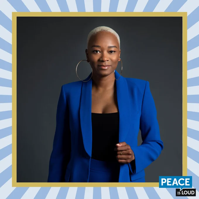 Headshot of Tiffany Dena Loftin, a young Black woman with cropped blonde hair, wearing a bright blue blazer and large gold hoop earrings.