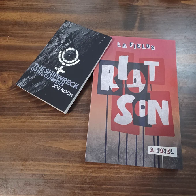 Paperback copies of The Shipwreck Of The Cerebus by Joe Koch and Riot Son by L. A. Fields on my kitchen table.