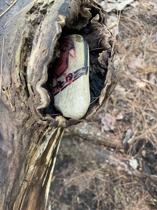 Someone has painted a cardinal on a small rock and left it in an fallen tree