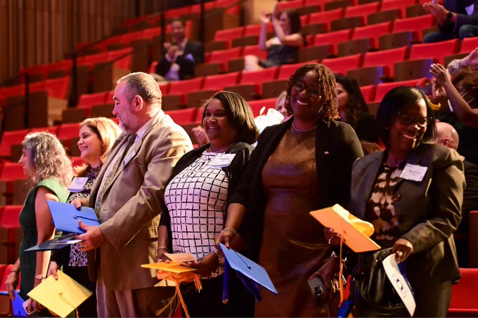 Family U participants holding multicolor grad caps and standing in front of an auditorium of red seats