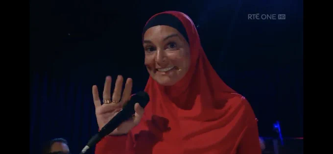 Sinead O’Connor, with microphone in hand, smiles and waves to the camera having finished singing Nothing Compares to You. She looks radiant.  