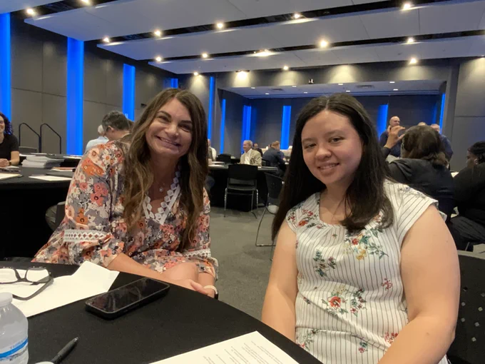 Two smiling women, Lena and Tech Services Director Jennifer Todd, are seated at a table in a conference room