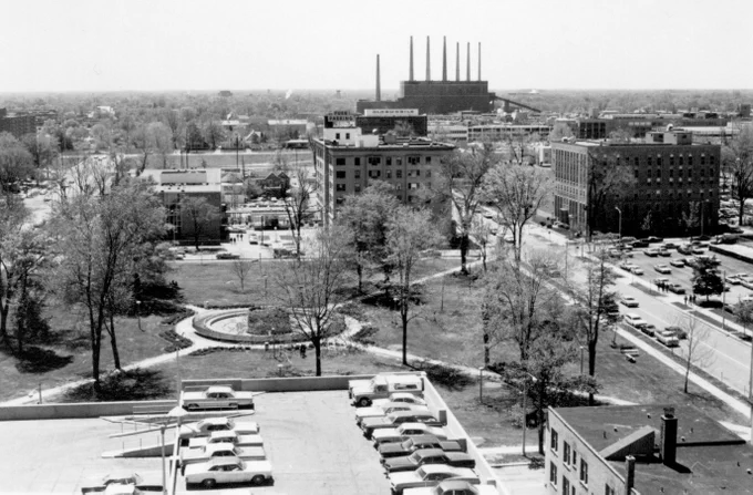 Black and white elevated view overlooking Reutter Park in Lansing. The top level of a parking garage is in the foreground and the Eckert Power Station with seven smokestacks is in the background.