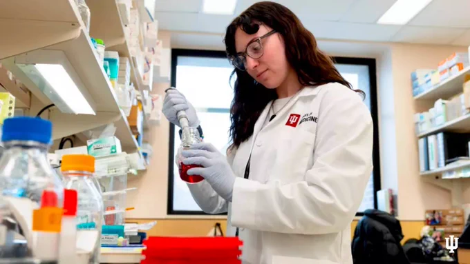 IUPUI junior Maddie Lisenko is pictured in white lab coat and latex gloves, working in a lab.
