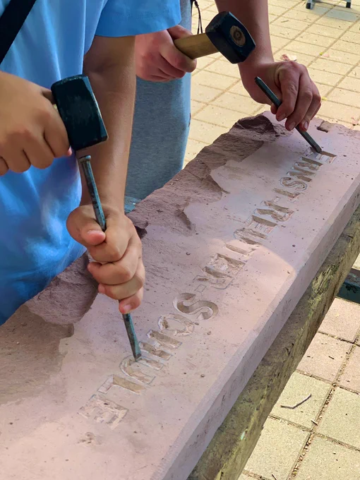In einen großen Stein meißeln zwei Schüler die Wörter “Ernst-Reuter-Schule”.