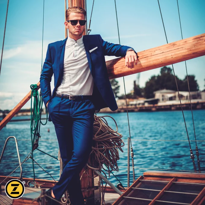 Man wearing a nice suit leaning against a sail on a sailboat. 