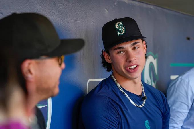 Photo of Jonny Farmelo in the dugout talking to local media. 