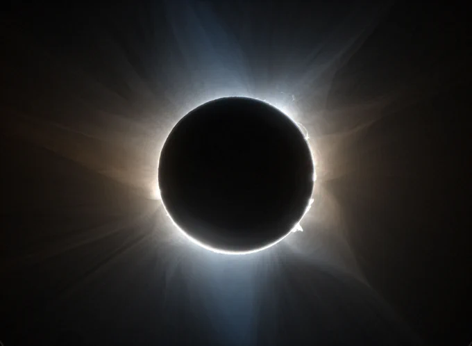 The Moon's shadow obscures the Sun, making the Sun appear like a black disk. The solar corona is emphasized and solar prominences are visible leaping from the surface. Dramatic whisps of solar energy emanate from the Sun. The rest of the image is dark. The  CATE 2024 team produced this view of the solar corona from images recorded in two polarization angles during a total solar eclipse in Australia on April 20, 2023. Credits: Courtesy of SwRI/Citizen CATE 2024/Dan Seaton