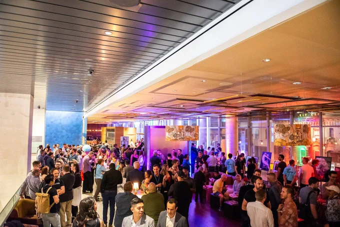 Photo of LUMA party space inside of TIFF Bell Lightbox. lots of people mingling and assorted coloured lighting. in the far background you can see out the floor to ceiling windows that it is night time.