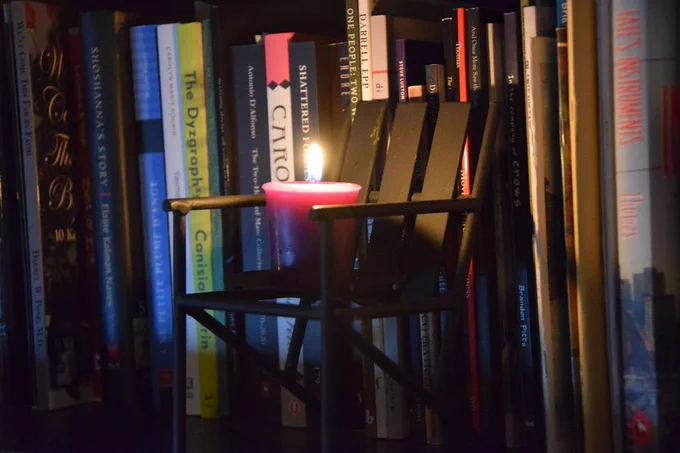 The cover banner for the lawn chair soirée publications party event on July 20, 2023. A photograph of Quebec writers' books (spines) with a little lawn chair in the foreground with a lit candle on the seat.
