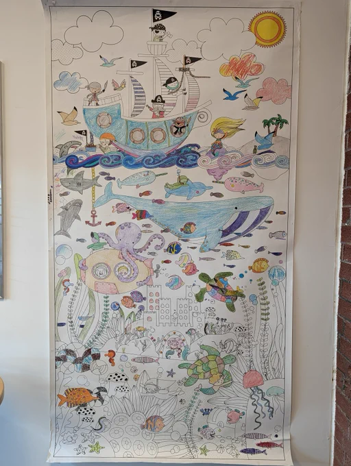 A large collaborative colouring page just inside the Charles Hall Library doors. The colouring sheet features a pirate ship, sea creatures, and an underwater city, with lots of open area still to be coloured. 