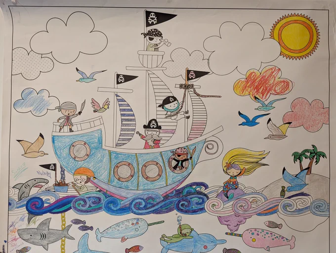 Top half of the colouring sheet just inside the Charles Hall Library doors, featuring pirates on a pirate ship, a mermaid, and several sea/sky creatures. Most of this part of the sheet has been coloured in, but some blank spots still remain in the clouds, sky, and pirate ship. 