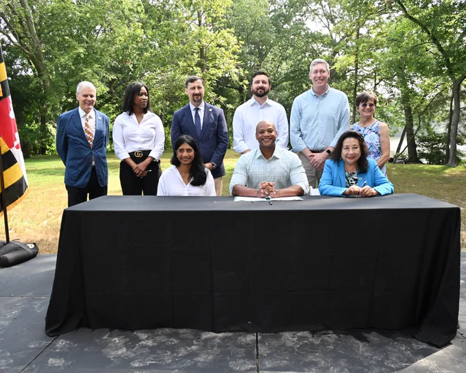 Governor Moore and Lt. Gov Aruna Miller posing for photo at table with others.