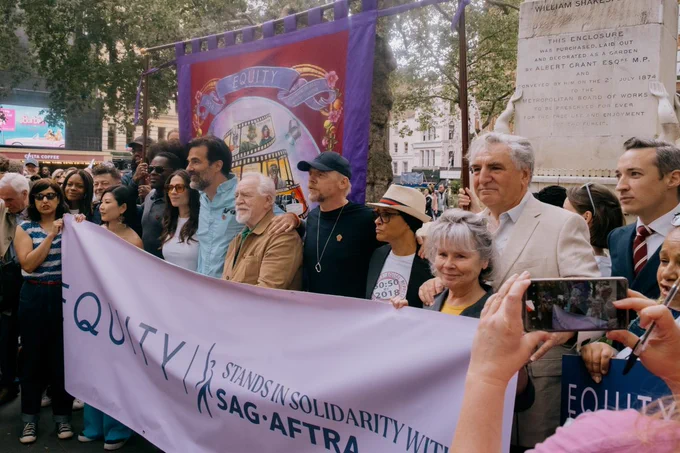 Photo shows from left to right: John McDonnell MP, Sonali Bhattacharyya, Naomie Harris OBE, Rebecca Yeo, Andy Serkis, David Oyelowo, Hayley Atwell, Rob Delaney, Brian Cox, Simon Pegg, Golda Rosheuvel, Imelda Staunton CBE, Jim Carter OBE and Paul W Fleming in London's Leicester Square holding large lavender banner that reads 'Equity Stands In Solidarity With SAG-AFTRA'.