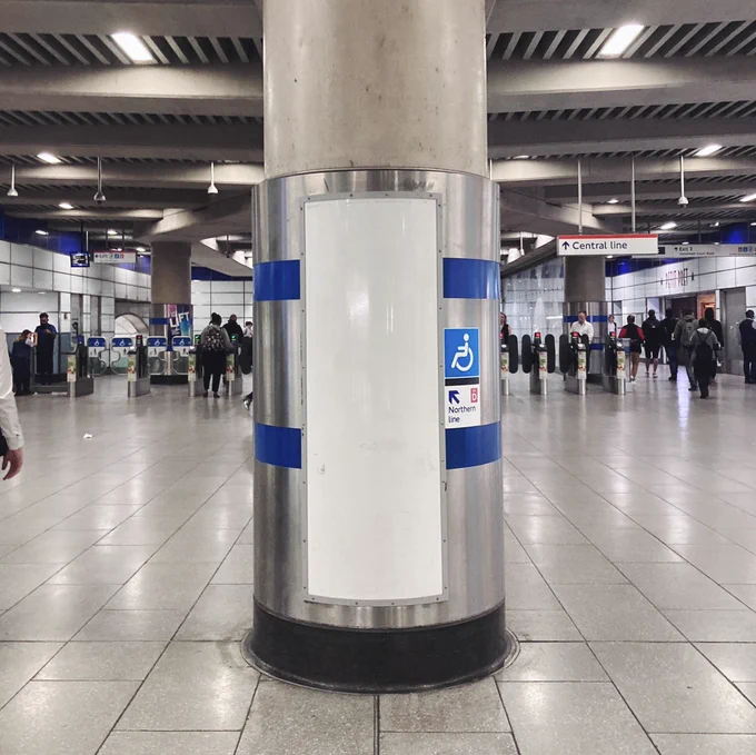 Photograph of an empty notice area on a pillar at Tottenham Court Road station, with people walking in the background.
