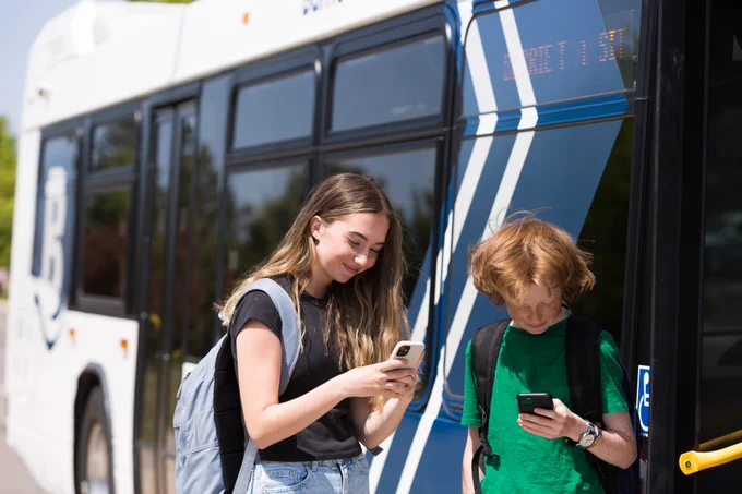 Two youths looking at their phones, getting on a city bus. 