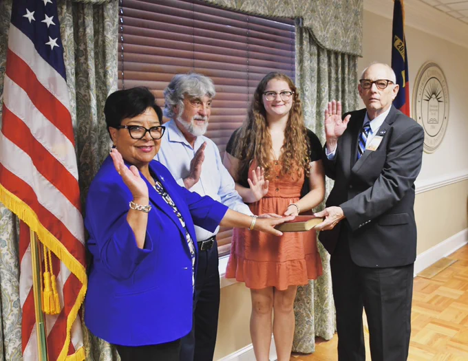 Four people in a board room taking an oath of office.