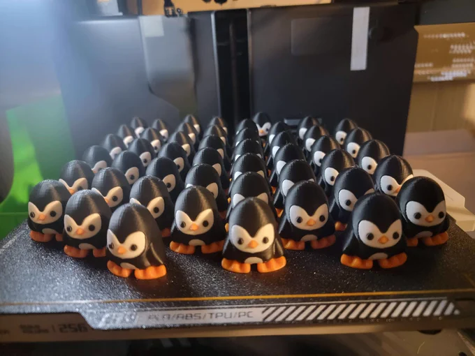 48 3D printed penguin chibimals are lined up 8 columns wide on a 3D printer build platform.