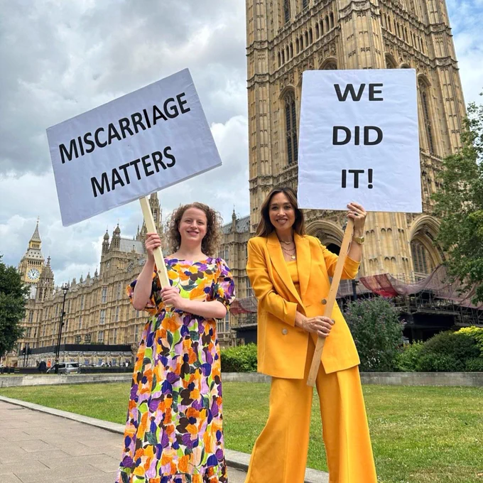 Olivia and Myleene standing outside Parliament with banners that say "Miscarriage Matters" and "We did it!"