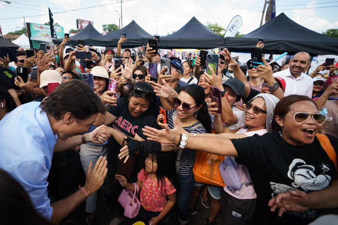 Prime Minister Justin Trudeau is crouching and high-fiving a young girl. A large crowd is people is standing in front of him.