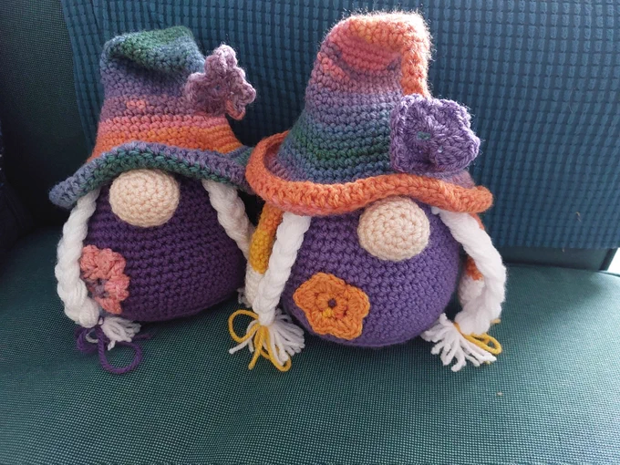 Two crochet gnomes with purple bodies, big noses, white plaits and big droopy multi coloured hats.
