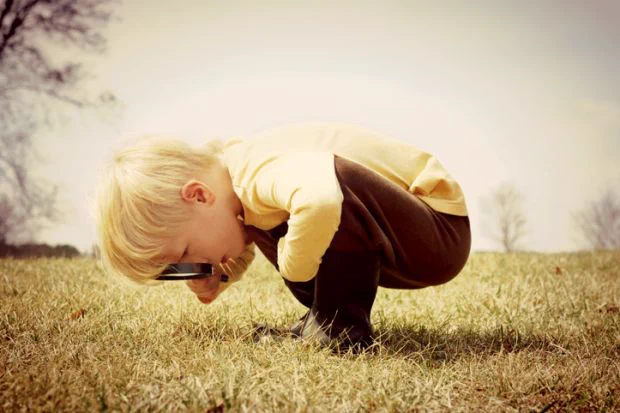 A very small boy bends double to look down at some grass with a magnifying glass