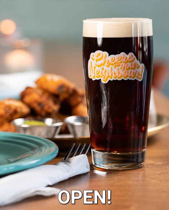 A photo of a glass of beer with a plate of wings in the background. The word: Open! Is written on the photo