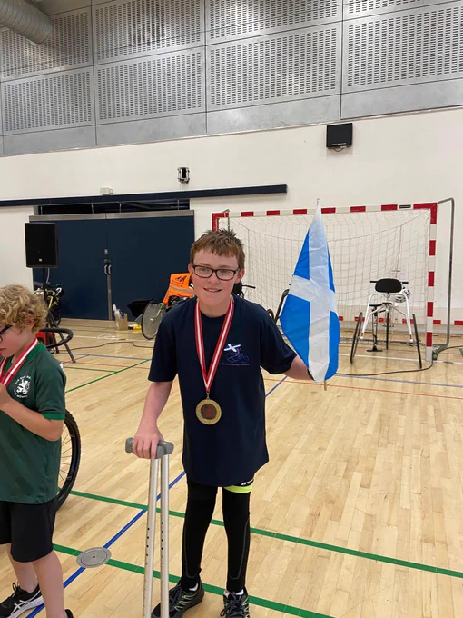 Iain standing with a scotland flag in his hand with his gold medal around his neck 