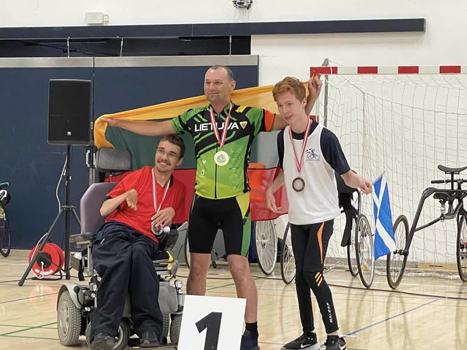 Matthew on the far right standing next to the other two athletes wearing his bronze medal and holding the Scotland Flag