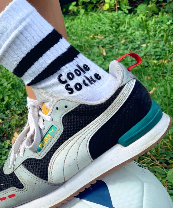 Der Fuß eines Schülers steht auf einem Ball. Auf seiner Sock steht „Coole Socke“.