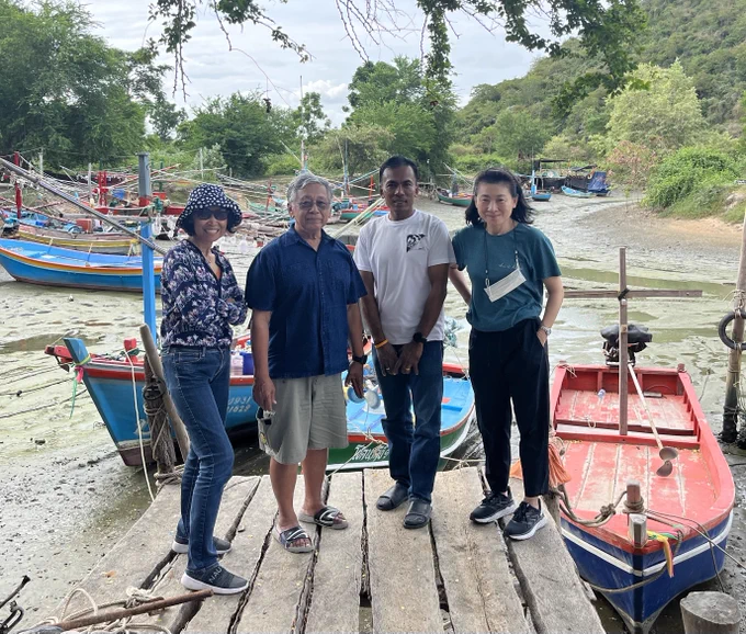 Geography professor Ratana Chuenpagdee with colleagues on a dock in Thailand. Small fishing boats are on a beach in the background. 