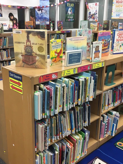 A bookshelf, chock full of children's books. Multiple children's books sit on top of the shelf as well.